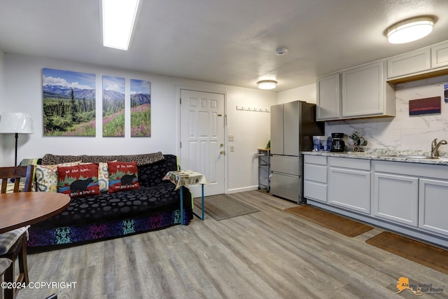 kitchen featuring decorative backsplash, sink, light stone countertops, light wood-type flooring, and stainless steel fridge