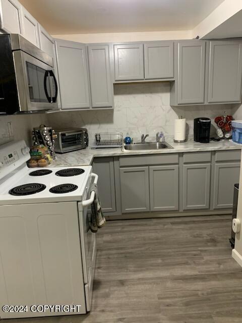 kitchen with sink, tasteful backsplash, white range with electric cooktop, wood-type flooring, and gray cabinets