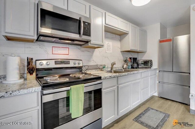 kitchen with white cabinetry, light stone counters, light hardwood / wood-style floors, and stainless steel appliances