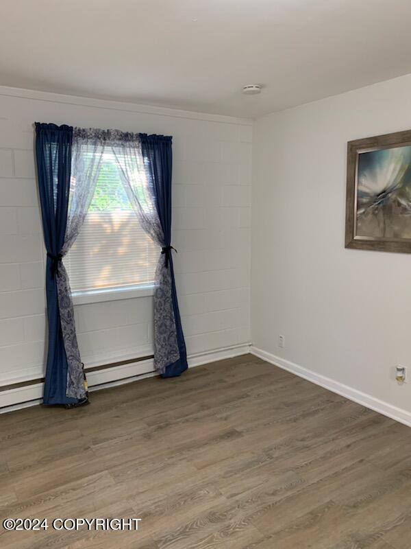 empty room featuring hardwood / wood-style floors and a baseboard heating unit