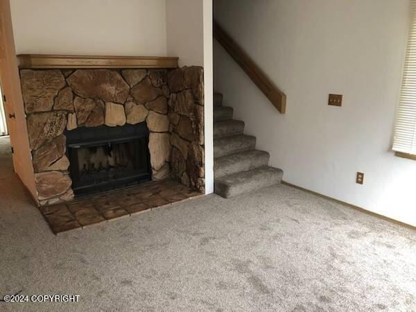 carpeted living room featuring a stone fireplace