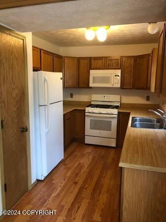 kitchen with dark wood-type flooring, white appliances, sink, and a textured ceiling