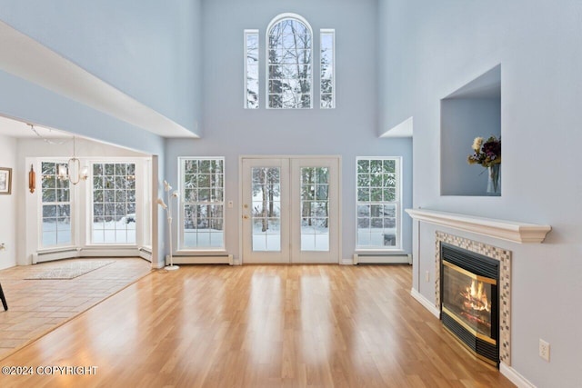 unfurnished living room with a high ceiling, light hardwood / wood-style flooring, a baseboard heating unit, and a notable chandelier