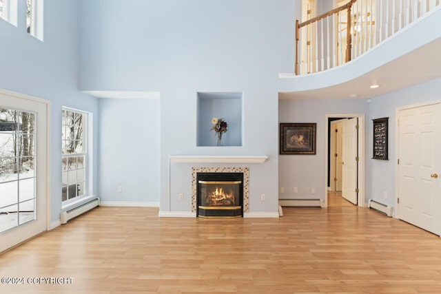 living room with a high ceiling, a tile fireplace, light hardwood / wood-style flooring, and a baseboard heating unit