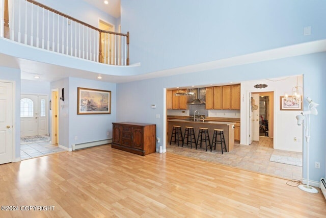 unfurnished living room featuring a high ceiling, light hardwood / wood-style flooring, sink, and a baseboard radiator