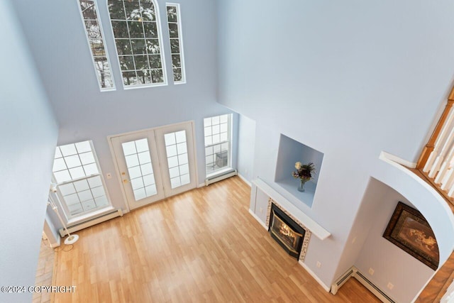 unfurnished living room with a stone fireplace, a towering ceiling, light hardwood / wood-style floors, and a healthy amount of sunlight