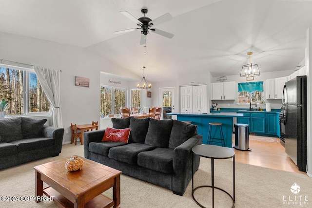 living room with light hardwood / wood-style floors, ceiling fan with notable chandelier, sink, and lofted ceiling