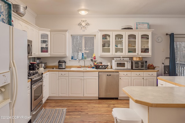 kitchen with ornamental molding, stainless steel appliances, white cabinetry, sink, and light hardwood / wood-style floors