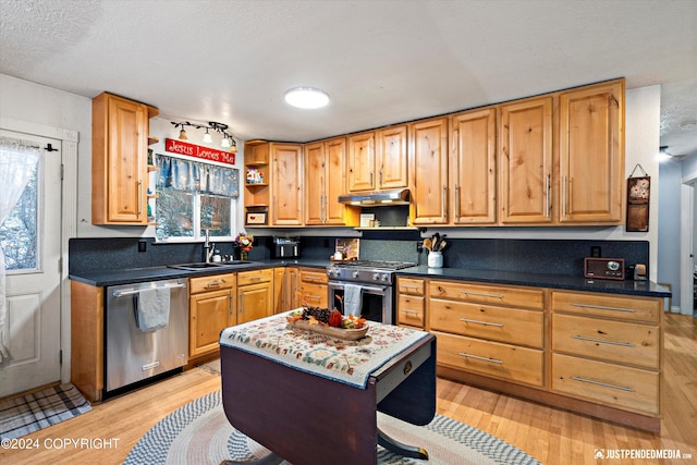 kitchen with stainless steel appliances, sink, a textured ceiling, light hardwood / wood-style flooring, and a center island