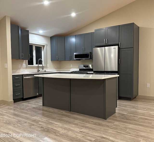 kitchen featuring sink, appliances with stainless steel finishes, vaulted ceiling, a kitchen island, and light wood-type flooring