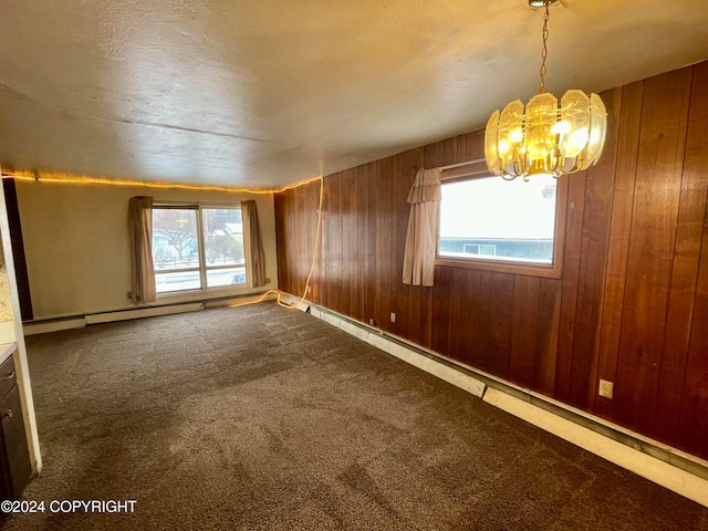 carpeted empty room featuring wooden walls, a baseboard heating unit, and an inviting chandelier