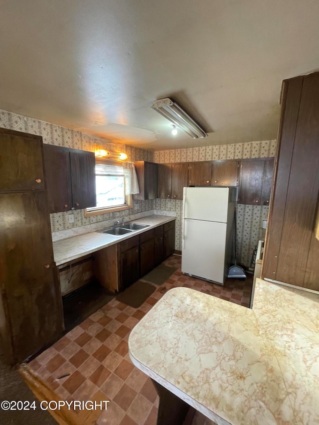 kitchen featuring decorative backsplash, kitchen peninsula, dark brown cabinets, sink, and white fridge