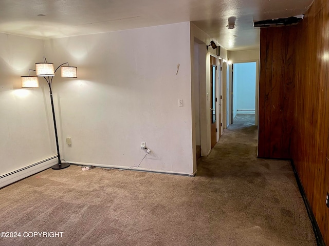 carpeted spare room featuring baseboard heating and wooden walls