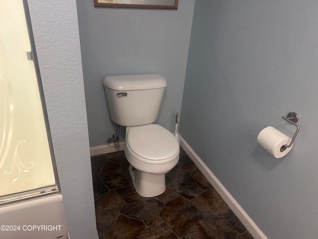 bathroom featuring toilet and bath / shower combo with glass door