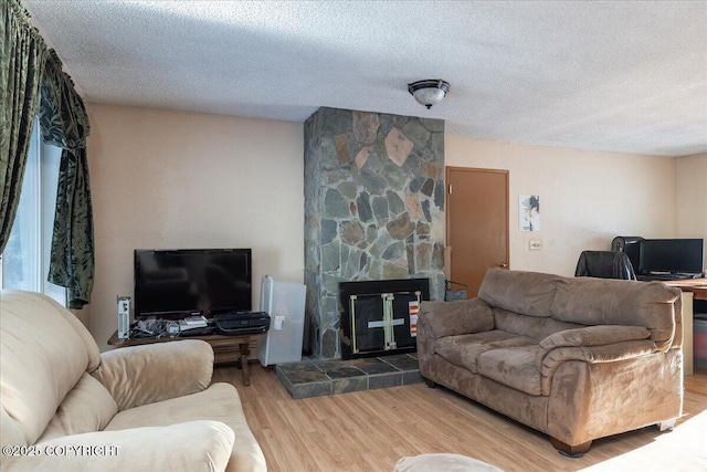 living room with a textured ceiling, a stone fireplace, and wood finished floors