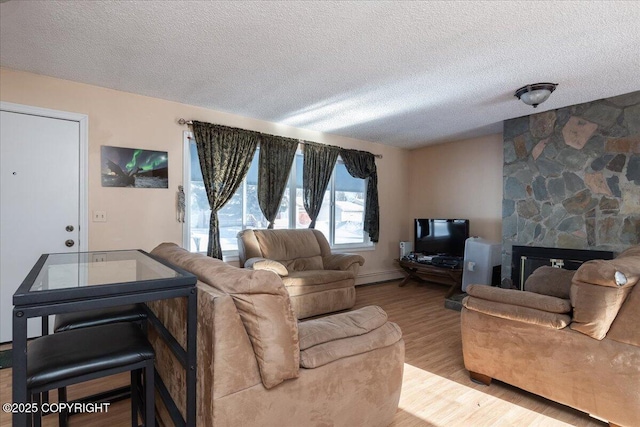 living room with a baseboard heating unit, a textured ceiling, a fireplace, and wood finished floors