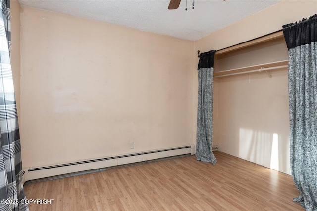 unfurnished bedroom featuring a baseboard heating unit, a ceiling fan, a textured ceiling, and wood finished floors