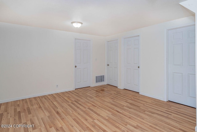 unfurnished bedroom featuring light wood-type flooring and multiple closets