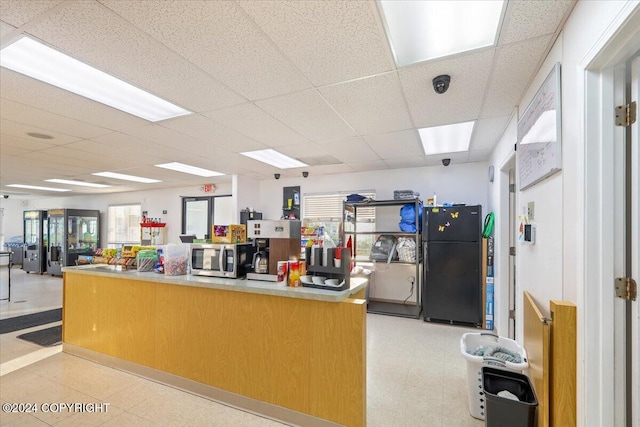 kitchen with black refrigerator, plenty of natural light, and a drop ceiling