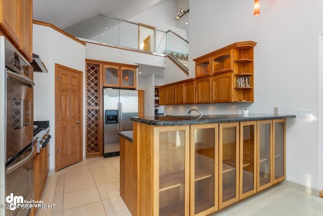 kitchen with light tile patterned floors, a towering ceiling, range hood, kitchen peninsula, and stainless steel appliances