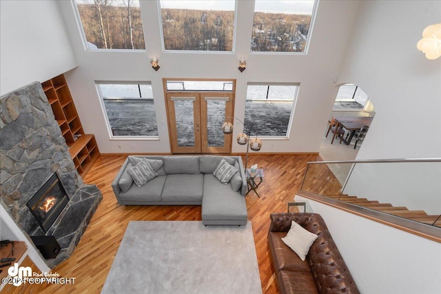 living room with a high ceiling, a stone fireplace, plenty of natural light, and hardwood / wood-style floors