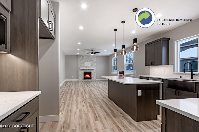 kitchen featuring dark brown cabinets, ceiling fan, sink, light hardwood / wood-style flooring, and a stone fireplace