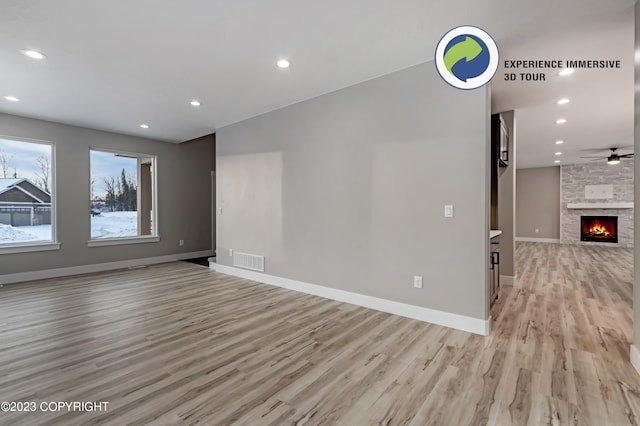 spare room featuring ceiling fan, a stone fireplace, and light hardwood / wood-style flooring