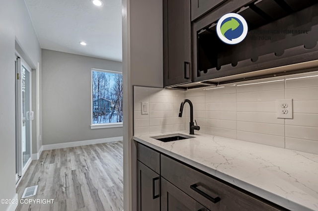 kitchen featuring light stone countertops, light wood-type flooring, tasteful backsplash, dark brown cabinetry, and sink