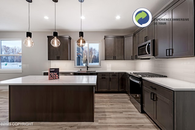 kitchen with light stone countertops, sink, decorative light fixtures, dark brown cabinets, and appliances with stainless steel finishes