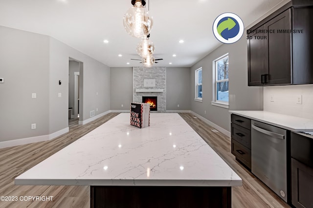 kitchen featuring dishwasher, a center island, light stone counters, and a fireplace