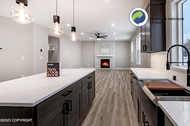 kitchen with ceiling fan, decorative light fixtures, a fireplace, light hardwood / wood-style floors, and a kitchen island