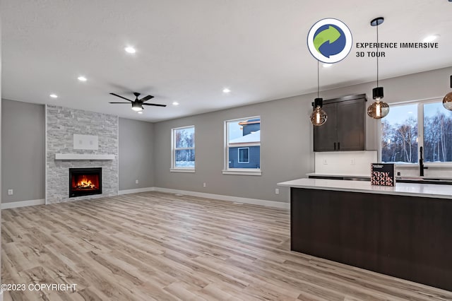 kitchen featuring dark brown cabinetry, ceiling fan, pendant lighting, light hardwood / wood-style flooring, and a fireplace