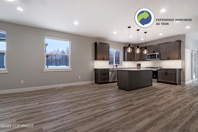 kitchen with appliances with stainless steel finishes, decorative light fixtures, a kitchen island, dark hardwood / wood-style flooring, and dark brown cabinets