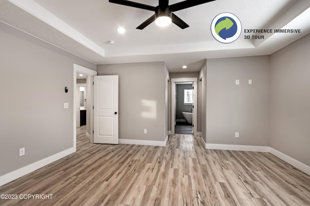 spare room featuring a raised ceiling, ceiling fan, and light hardwood / wood-style flooring