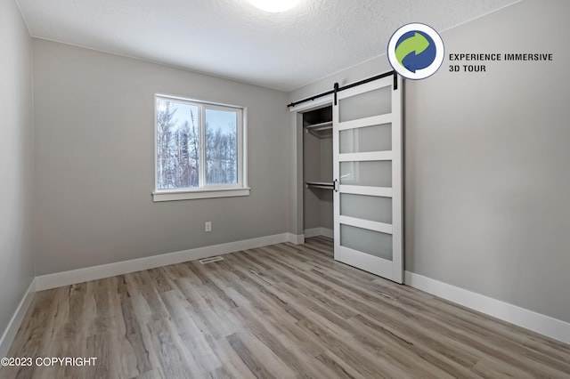 unfurnished bedroom featuring a textured ceiling, a barn door, light hardwood / wood-style floors, and a closet