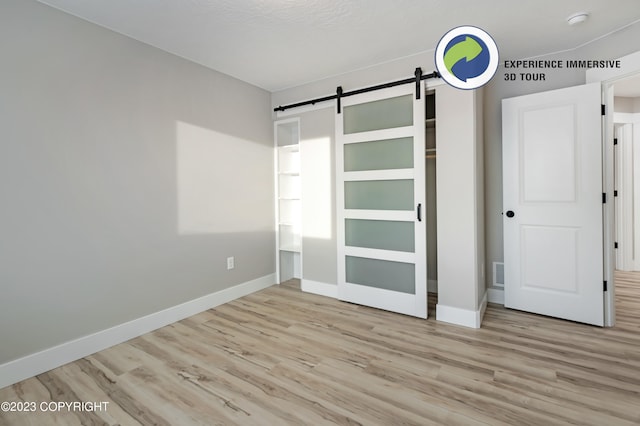 unfurnished bedroom with a barn door, light hardwood / wood-style floors, and a closet