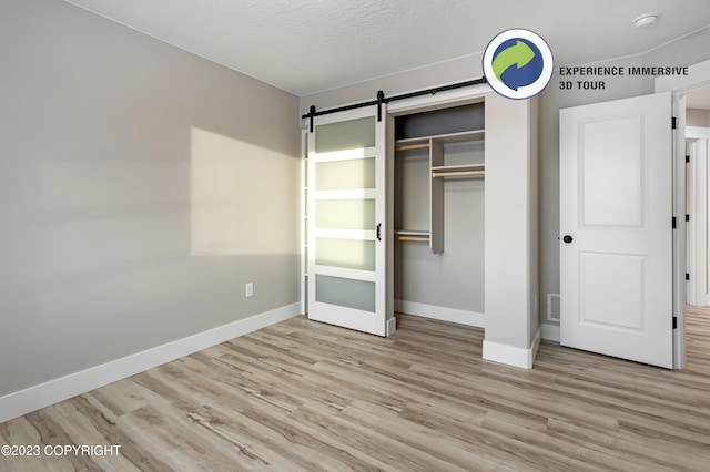 unfurnished bedroom featuring a barn door, a closet, and light wood-type flooring