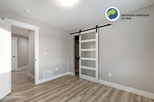 unfurnished bedroom with a barn door and light wood-type flooring