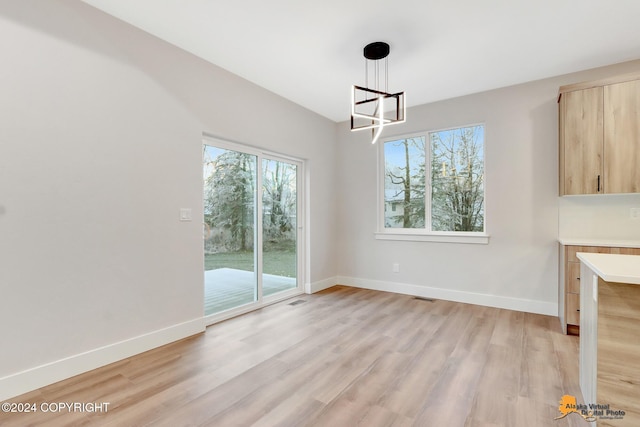 unfurnished dining area with light wood-type flooring and an inviting chandelier