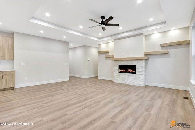 unfurnished living room featuring ceiling fan, light hardwood / wood-style flooring, a raised ceiling, and a fireplace