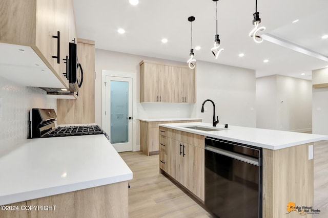 kitchen featuring decorative light fixtures, light brown cabinetry, stainless steel gas stove, and an island with sink