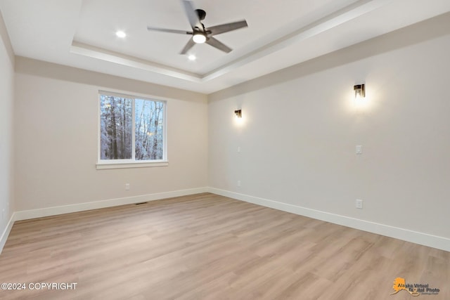 empty room with ceiling fan, a tray ceiling, and light hardwood / wood-style flooring