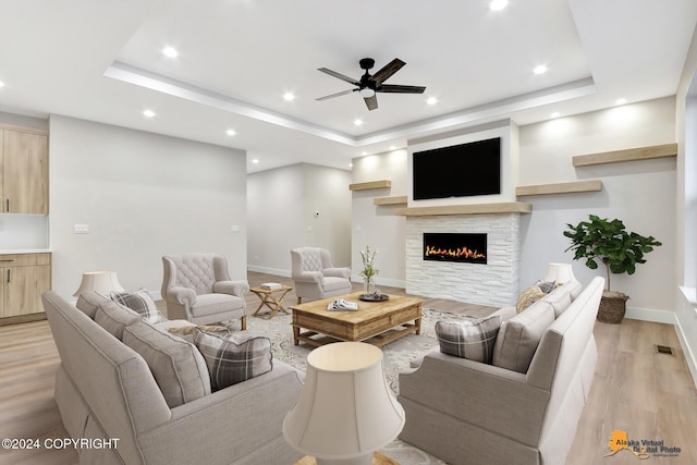 living room with ceiling fan, light wood-type flooring, a fireplace, and a tray ceiling