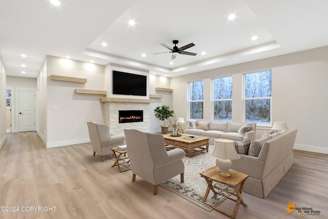 living room with a fireplace, light hardwood / wood-style floors, a tray ceiling, and ceiling fan