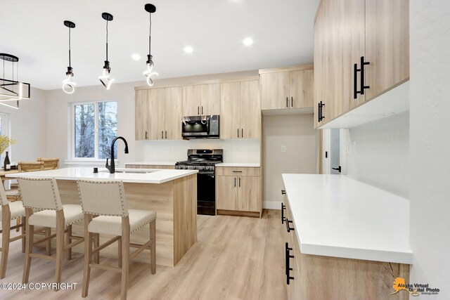 kitchen with appliances with stainless steel finishes, sink, light brown cabinets, and a kitchen island with sink