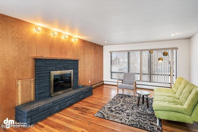 living room with a fireplace, a baseboard heating unit, hardwood / wood-style flooring, and wooden walls