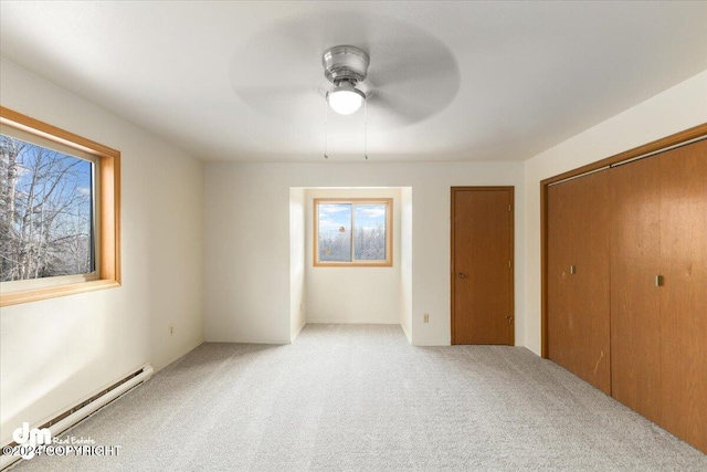 unfurnished bedroom featuring multiple windows, ceiling fan, light carpet, and a baseboard heating unit