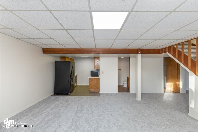 basement with a paneled ceiling and black refrigerator with ice dispenser