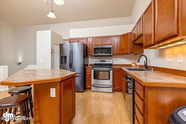 kitchen featuring a kitchen island, appliances with stainless steel finishes, hanging light fixtures, sink, and light hardwood / wood-style flooring