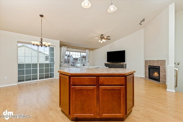 kitchen featuring a tiled fireplace, ceiling fan with notable chandelier, light hardwood / wood-style flooring, lofted ceiling, and pendant lighting